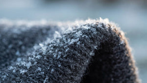 Gros plan d'une maille en laine mérinos gris anthracite recouverte de cristaux de givre